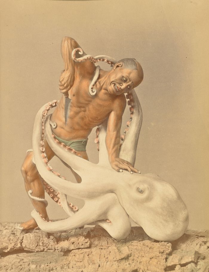 Vintage photograph of a man wrestling with an octopus on a rocky shore.