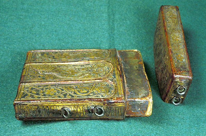 Two antique books with ornate metal covers on a green fabric background.
