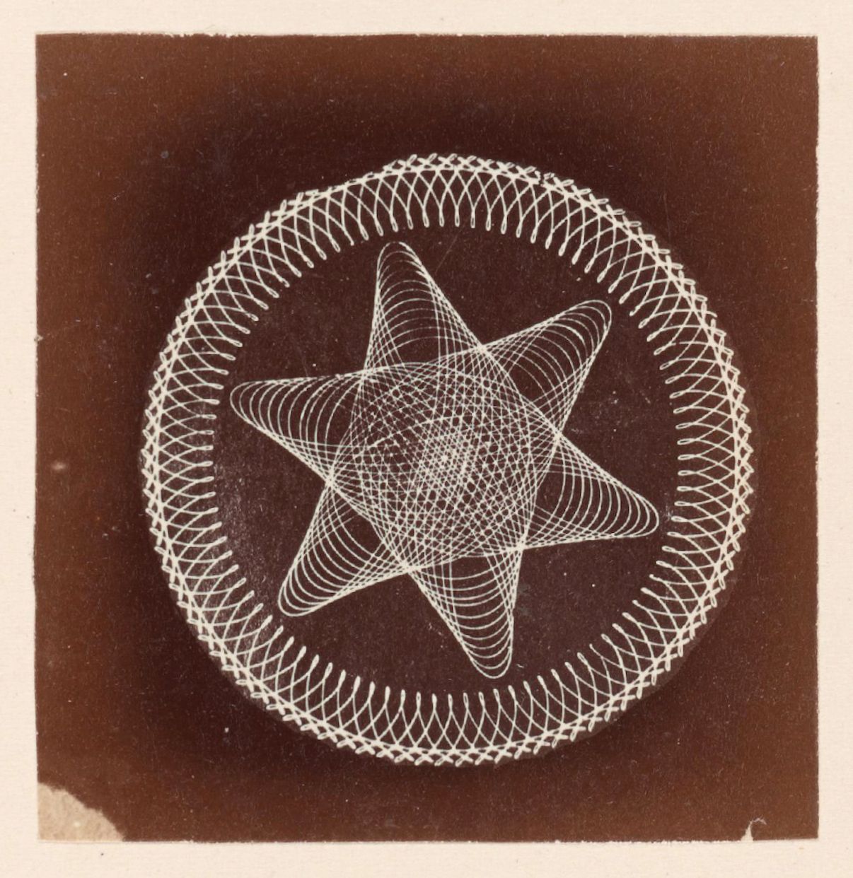 A vintage photograph of a geometric pattern featuring a five-pointed star surrounded by a circular design made of curved lines.