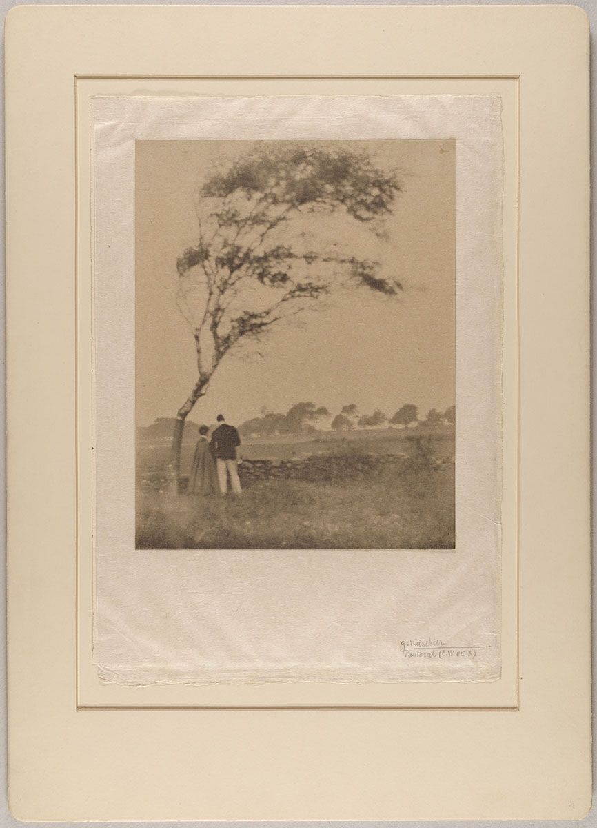 Sepia-toned photograph of a landscape with two figures standing near a tree.