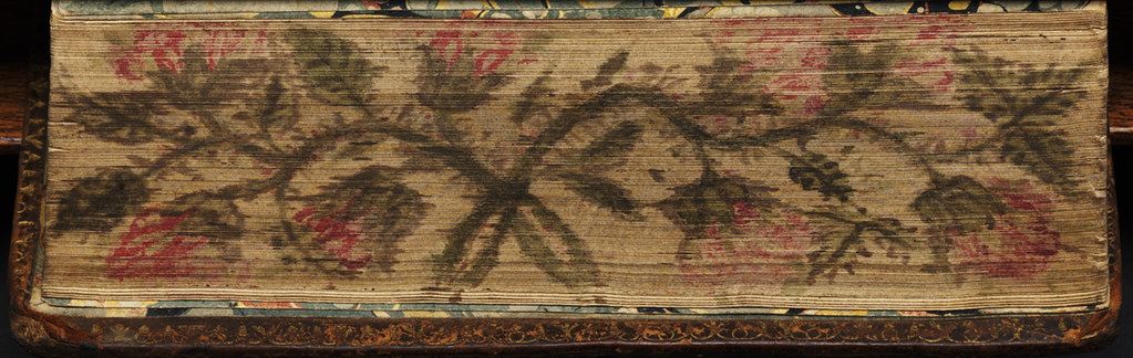 Close-up of a very old book cover with a faded floral pattern and gold trim.