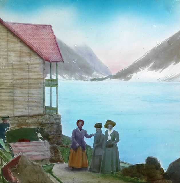 Vintage hand-colored photograph of a landscape with a building, people, and a body of water.