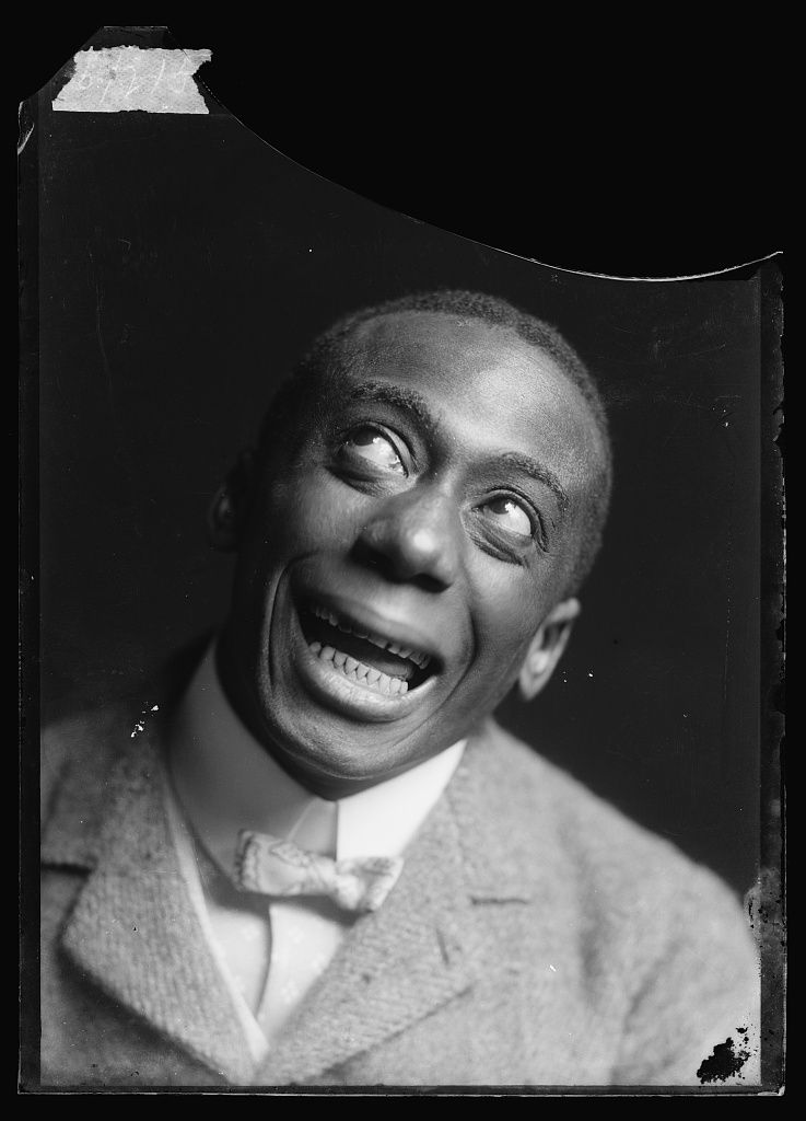 A black and white portrait of a man with a wide, exaggerated smile.