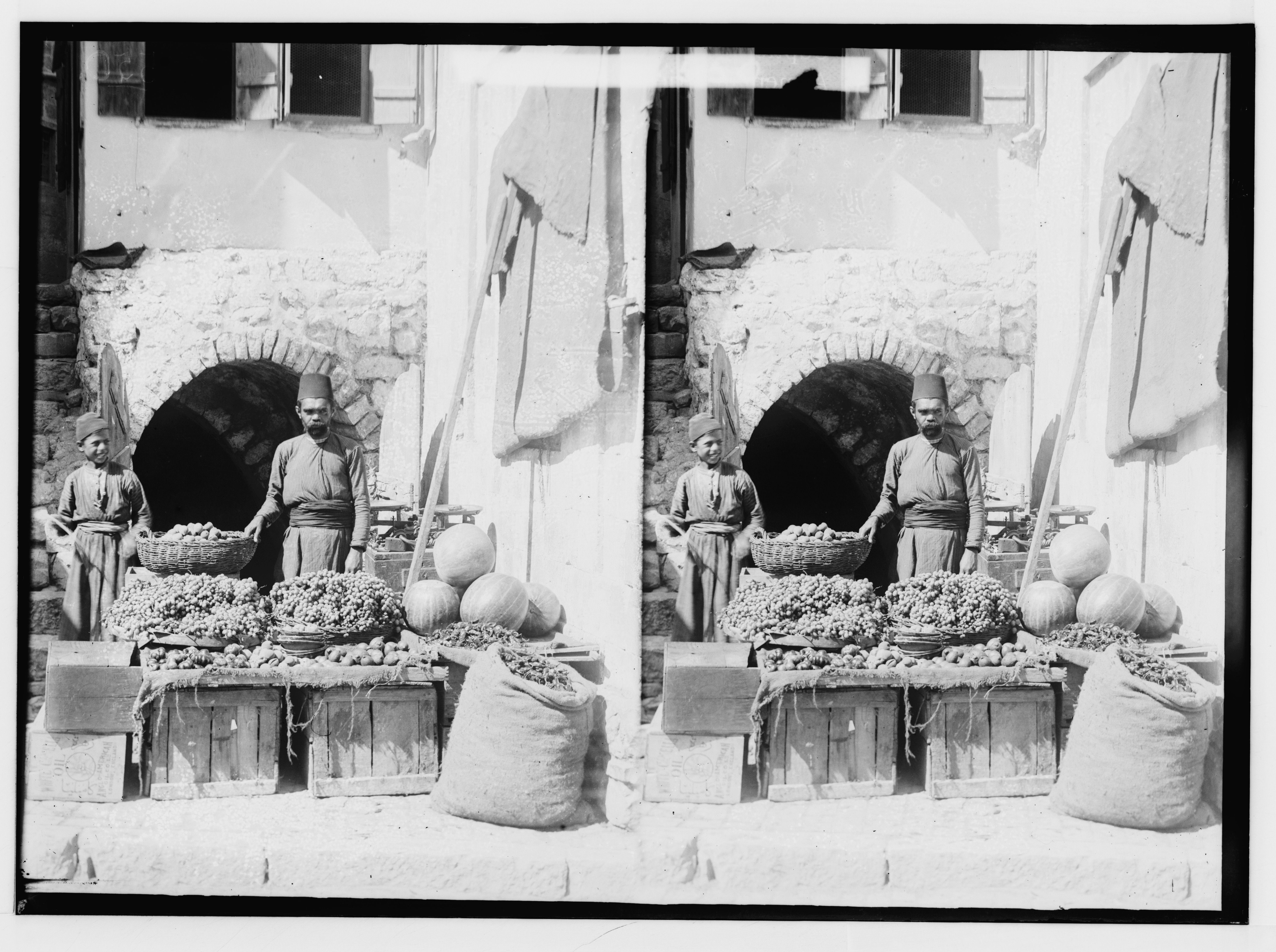 Stereoscopic photograph of a market stall with vendors and produce in an arched alcove of a stone building.