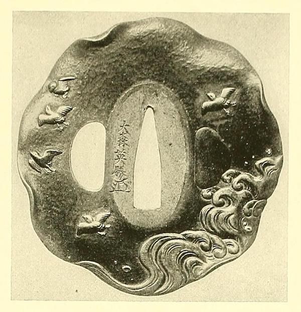 A vintage black and white image of a Japanese tsuba adorned with birds and Japanese writing.