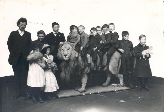 A vintage black and white photograph of a group of children posed around and on top of a taxidermied lion.