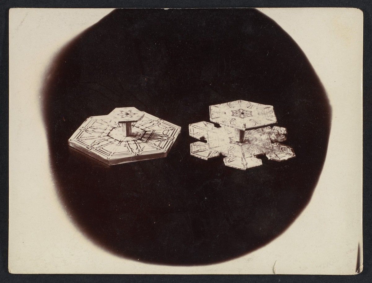 Vintage black and white photograph of two snowflakes against a dark background.
