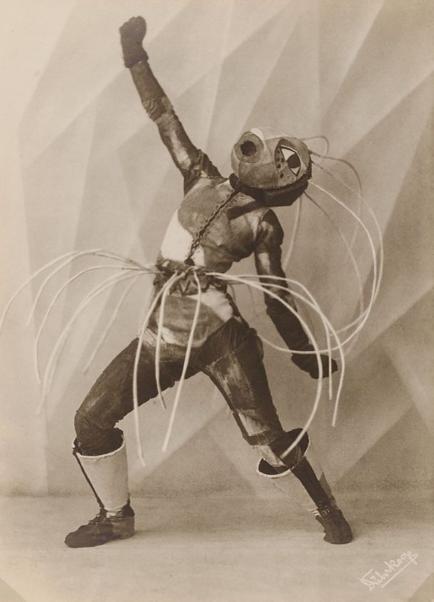 A vintage black and white photograph of a person dressed in an elaborate ant costume, posed dramatically against a geometric background.