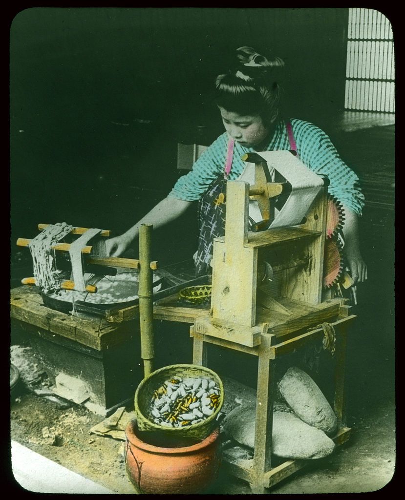 A woman working with a silk reeling machine, surrounded by silk cocoons and traditional tools.