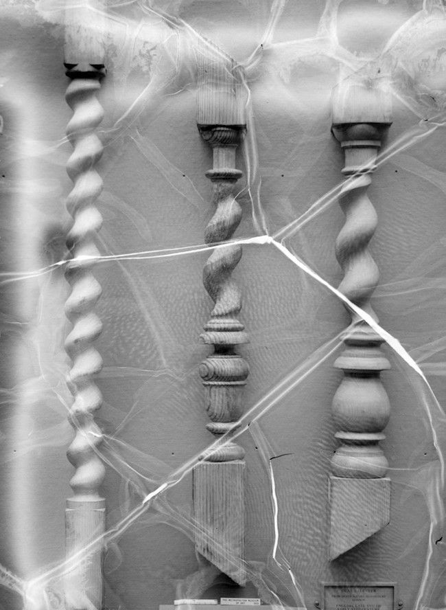 A black and white photograph of three antique table legs with a spiderweb draped across them.