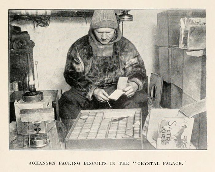 A black and white photograph of Johansen packing biscuits in the "Crystal Palace". The person is seated at a table, focused on the task of packing small, rectangular biscuits into individual paper sleeves.