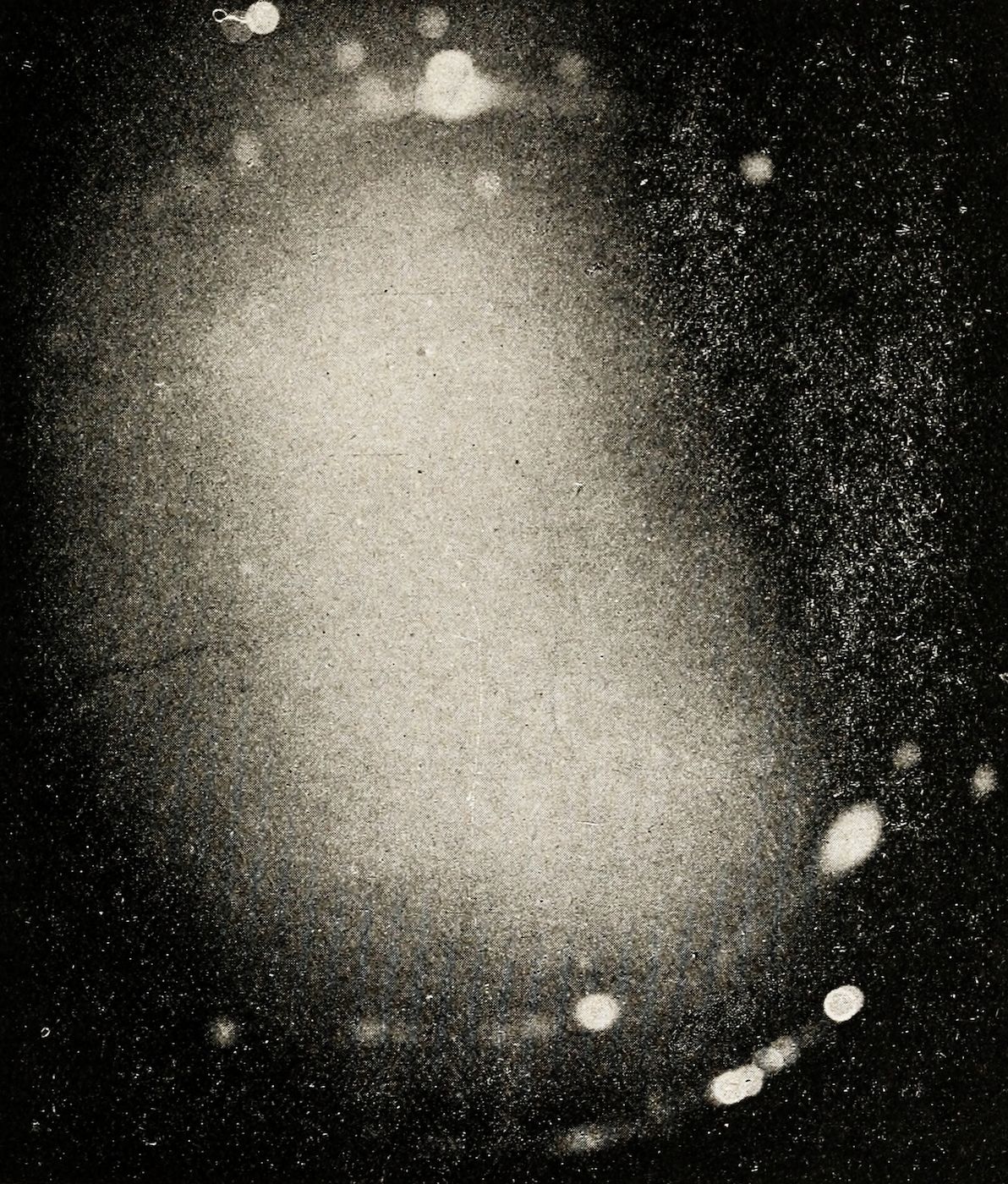 A grainy, black and white photograph of a spiral galaxy with a bright central core and numerous stars and dust particles.