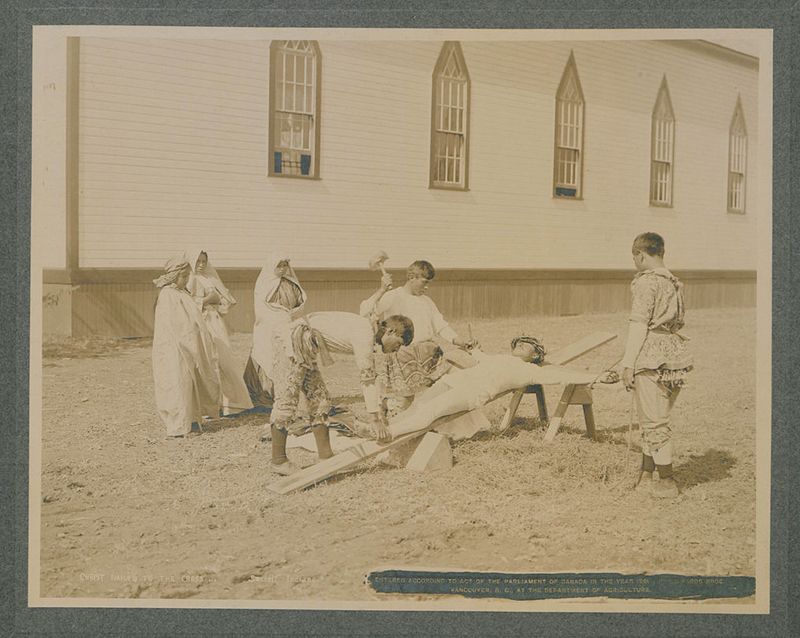 A sepia-toned vintage photograph of a group of people gathered outdoors in front of a wooden building, with a cannon or large weapon on a makeshift table in the center.