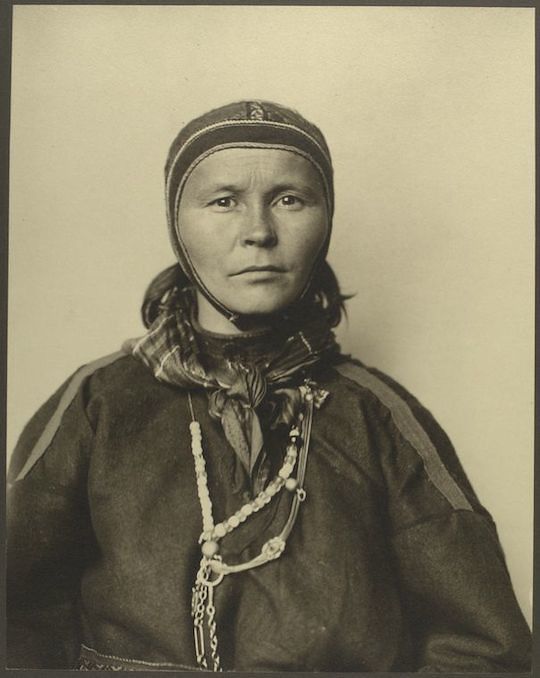 A vintage sepia-toned portrait of a woman wearing a head covering and beaded necklace.
