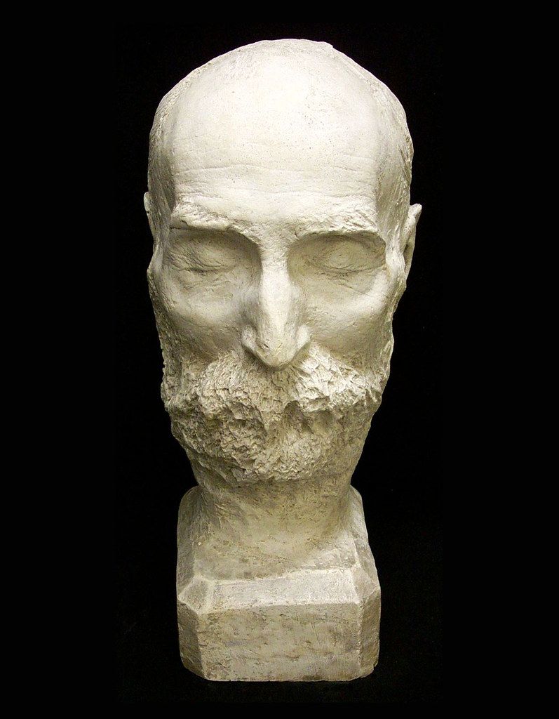 A plaster bust of a bald, bearded man against a black background.
