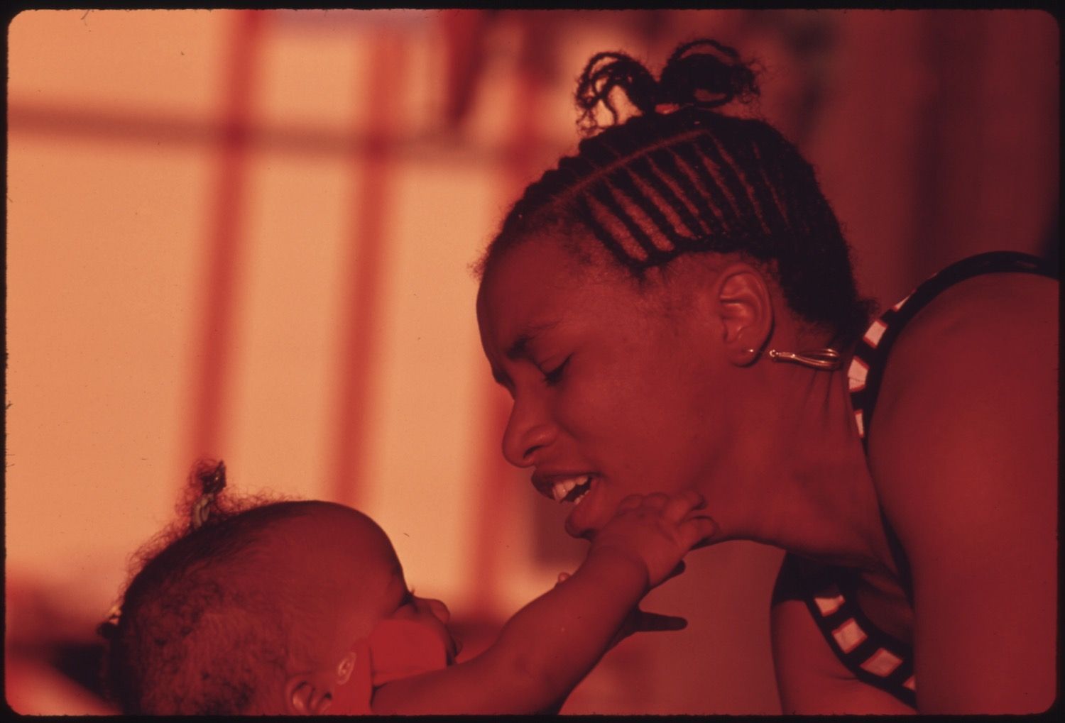 Close-up of a woman looking down at a baby in a warm, red-toned image.