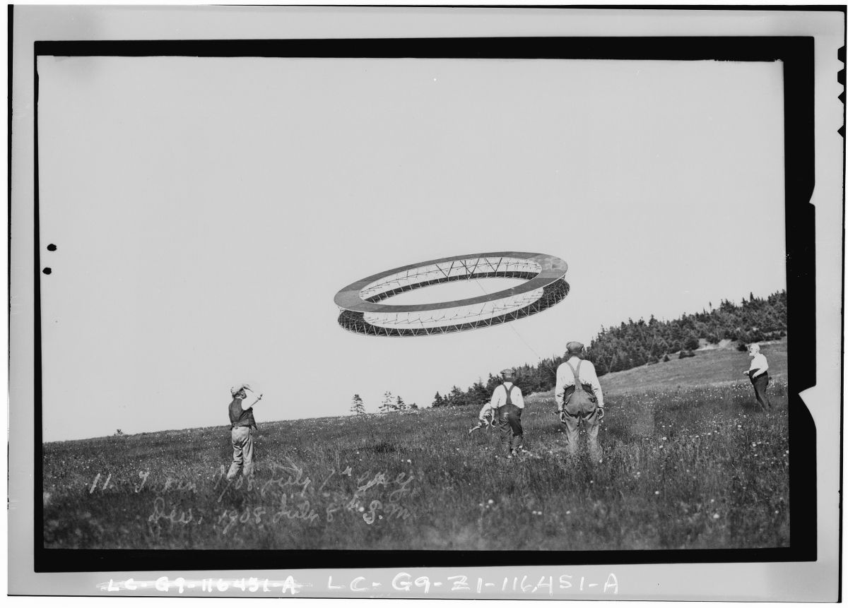 A black and white photograph of a UFO hovering over a grassy hill with people observing it.