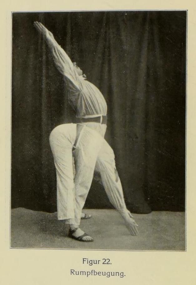 A vintage photograph of a person performing a forward bend stretching exercise, wearing light-colored clothing and barefoot on a dark floor.