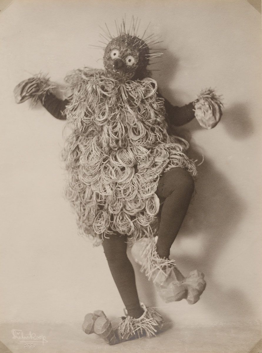 A vintage sepia-toned photograph of a person wearing a straw costume, posed in a dynamic stance.