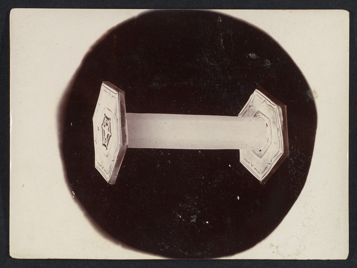 A black and white photograph of a white geometric object resembling a dumbbell or hourglass shape centered within a large black circle.