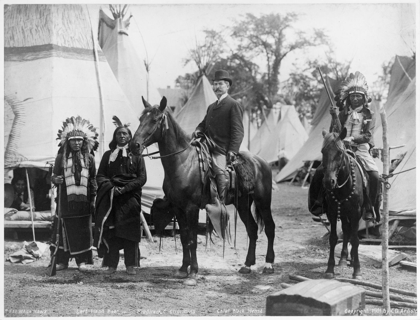 A vintage black and white photograph depicting a scene with Native American individuals and a man on horseback.
