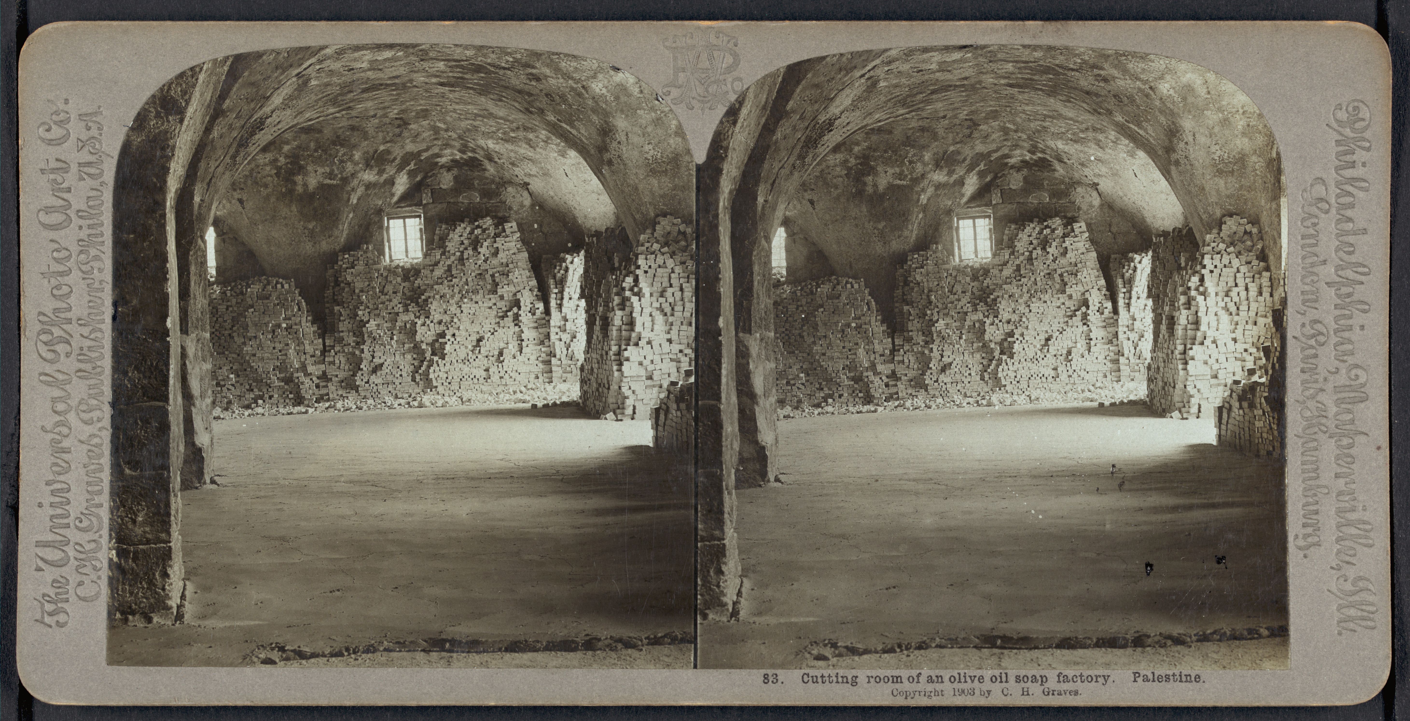 Stereoscope card of the cutting room of an olive oil soap factory in Palestine, showing a large room with stone pillars, workers on the floor, and a small window providing light.