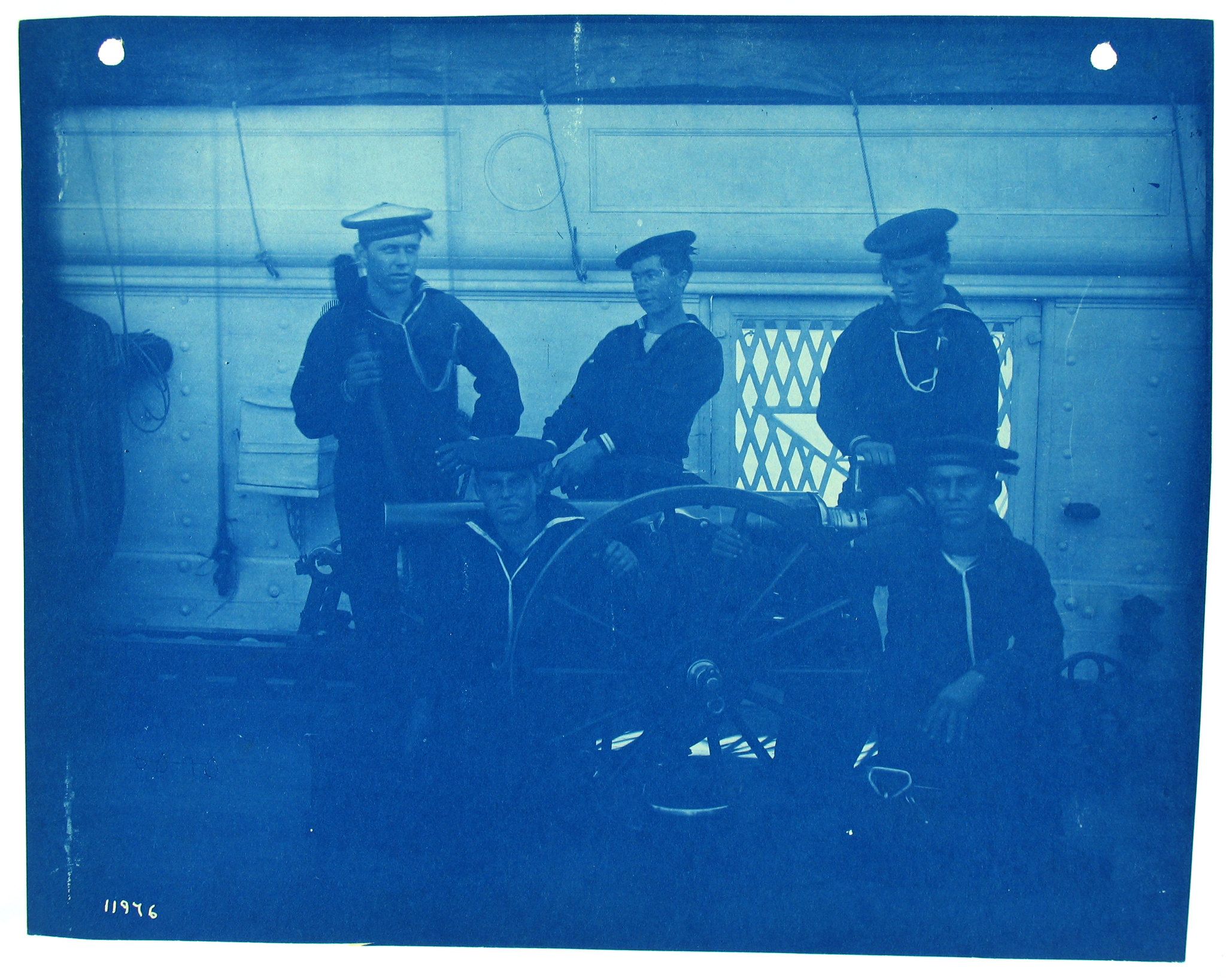 Cyanotype photograph of four sailors standing around a large gun on a ship.