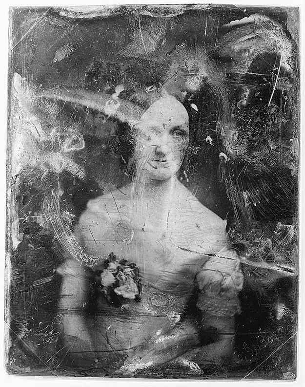 A vintage daguerreotype portrait of a woman with scratches and abrasions.