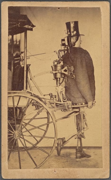 A sepia-toned photograph of a man fused with a complex steam-powered machine, dressed in formal attire with a top hat and long coat, operating a carriage-like vehicle with a large spoked wheel.