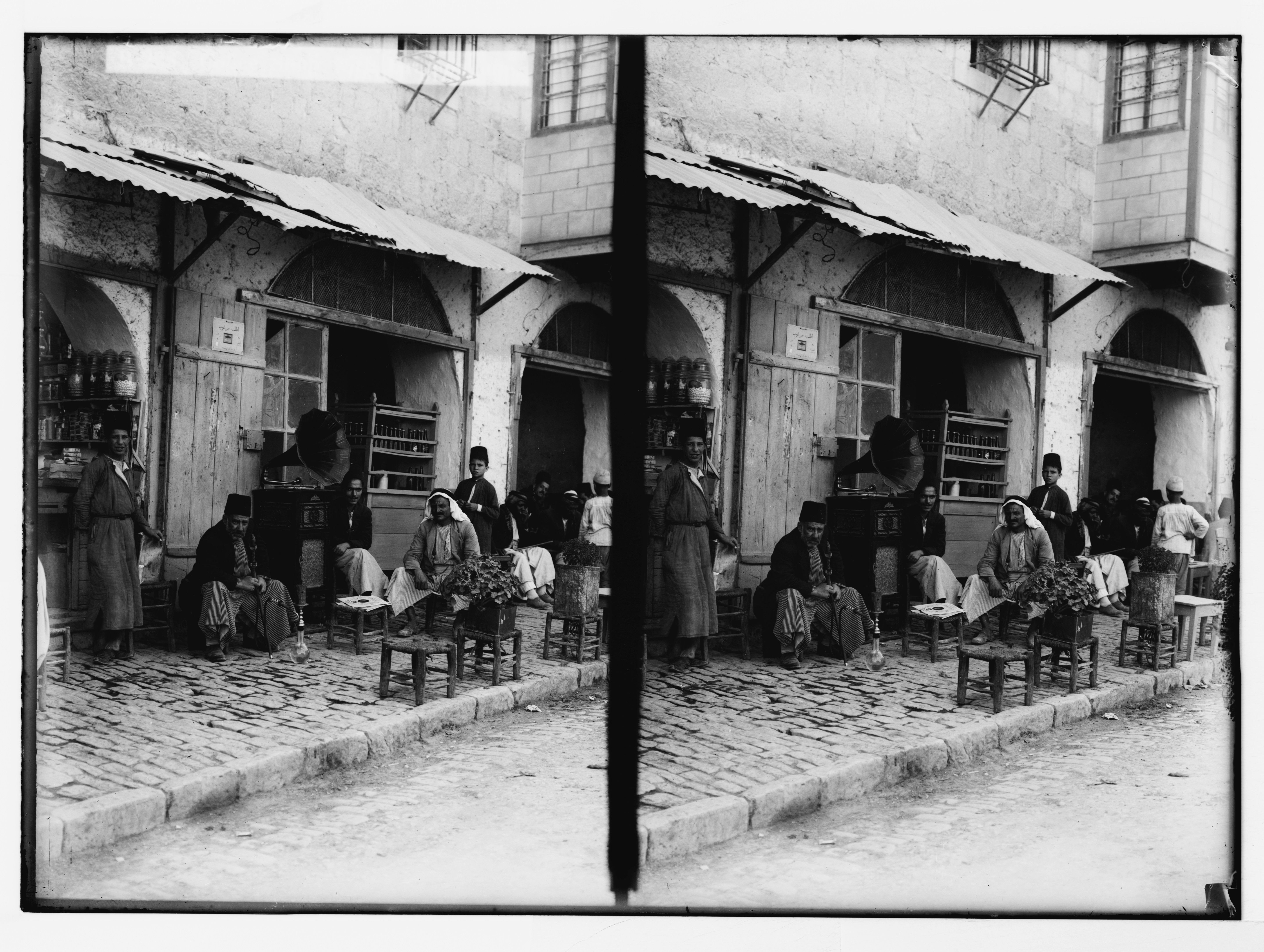 Stereoscopic photograph of a street scene with a storefront and people gathered outside.