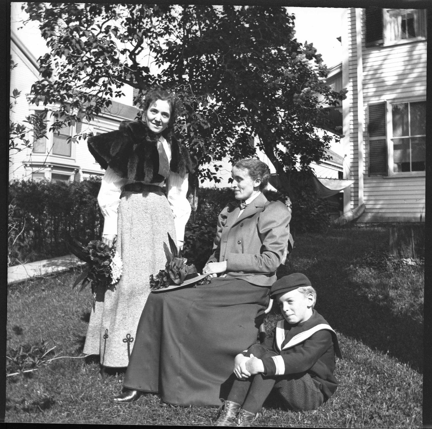 Black and white photograph of three people posing outdoors in front of a house.