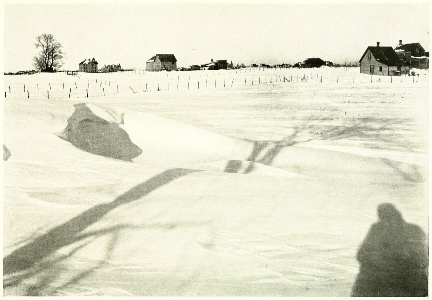 A black and white photograph of a snowy landscape with shadows of a person and a sled.